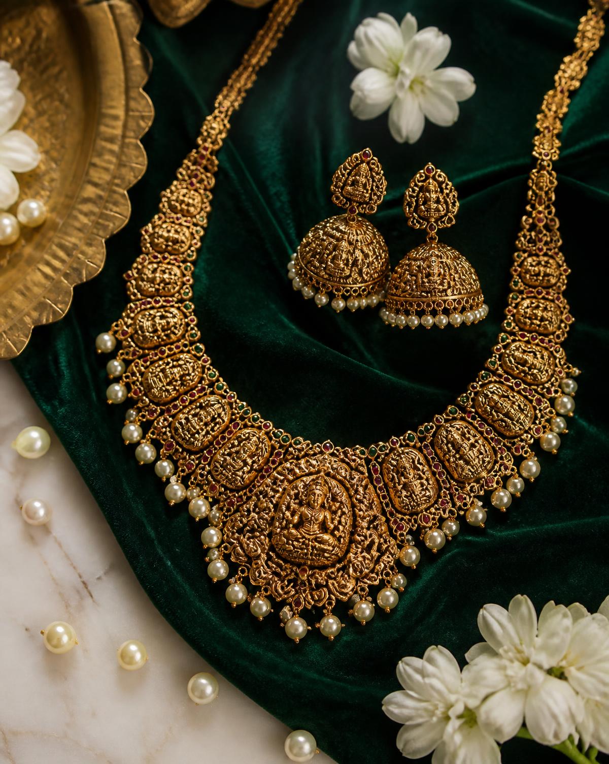 Antique gold temple necklace and jhumkas laid on emerald velvet with a brass tray